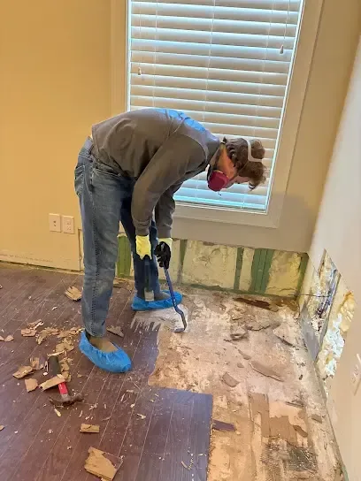Wet flooring pulled up along a wall that was cut open at the bottom for drying
