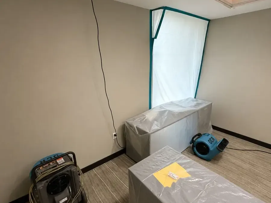 Air movers behind a plastic containment wall drying out an emptied room