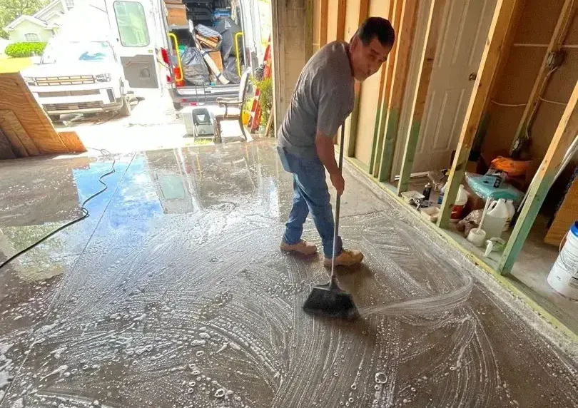 Homeowner sweeping muddy storm water out of a house toward an open garage door