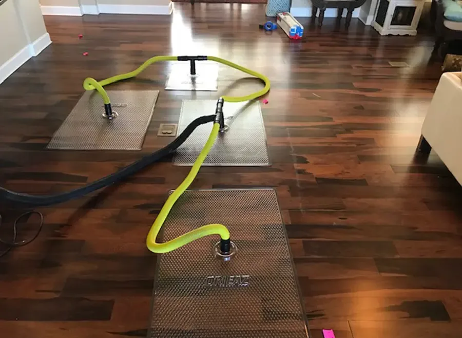 Floor drying mats connected to yellow vacuum hoses on a wet hardwood floor